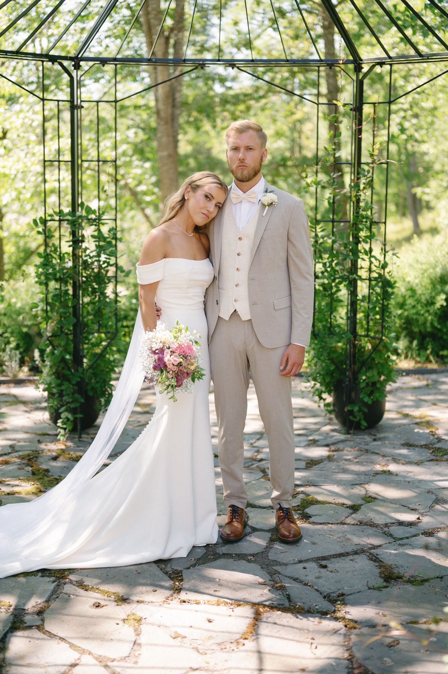 Romantic wedding photos taken under garden gazebo with climbing vines and stone path.