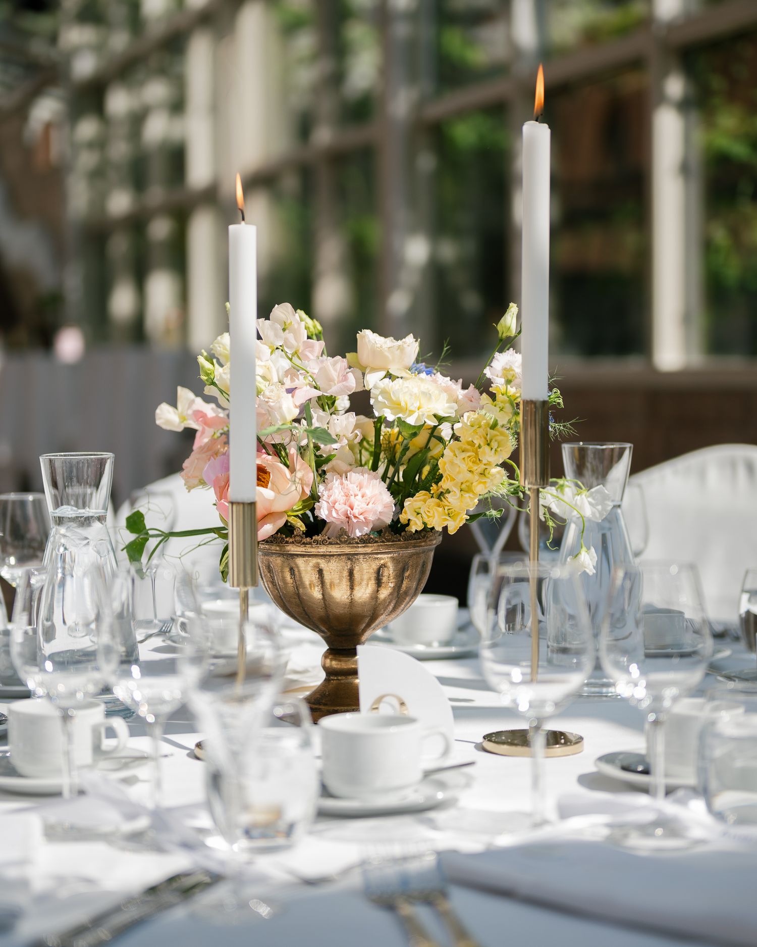Elegant wedding table centerpiece with white taper candles, blush pink and yellow flowers in a gold urn vase.