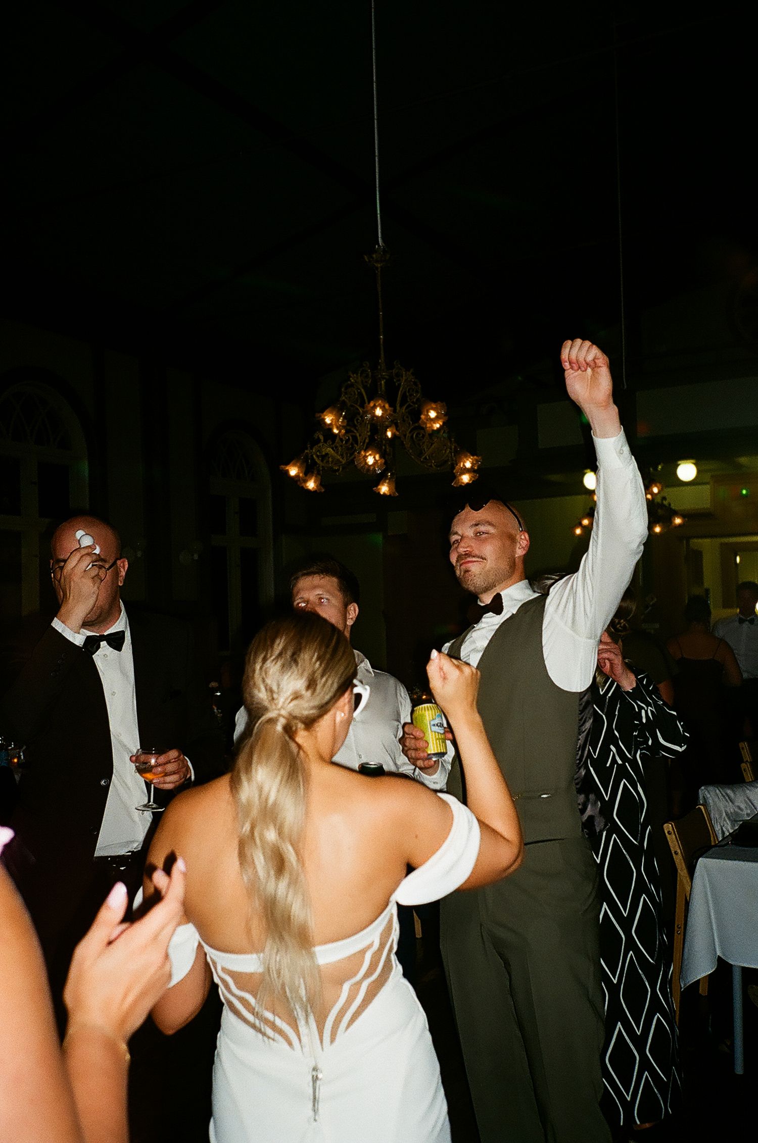 Wedding reception dance party with guests celebrating under hanging lights.