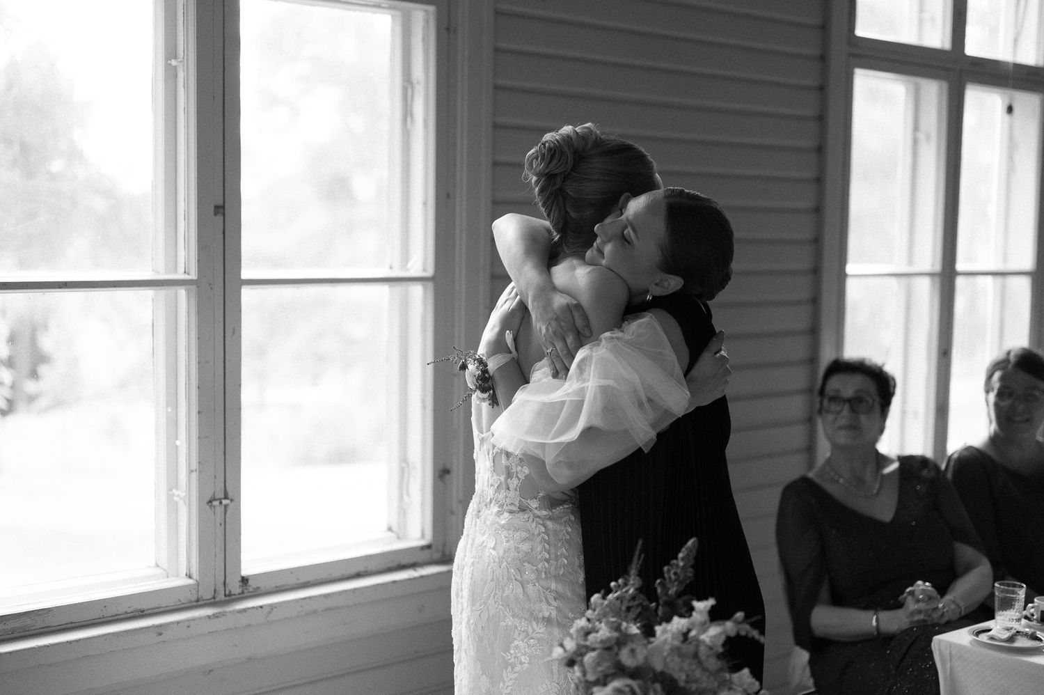 A tender embrace shared during a wedding celebration near bright windows.