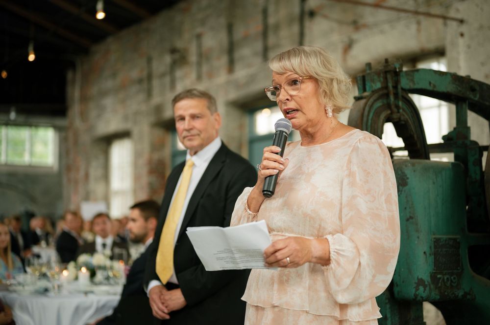 Wedding guests enjoying speeches and toasts during an indoor reception.