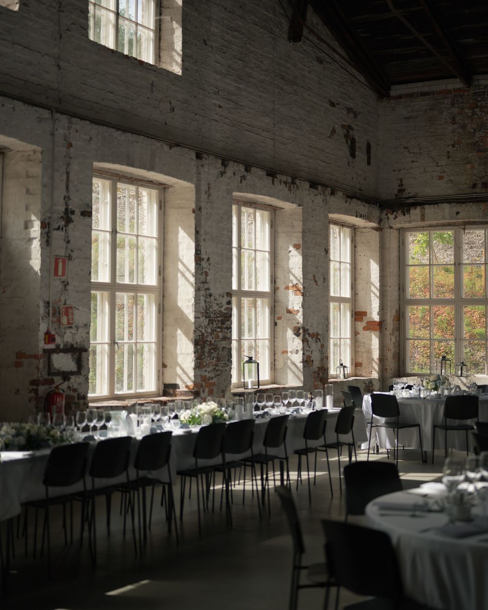 Large industrial venue with exposed brick walls and windows streaming natural light onto dining tables.