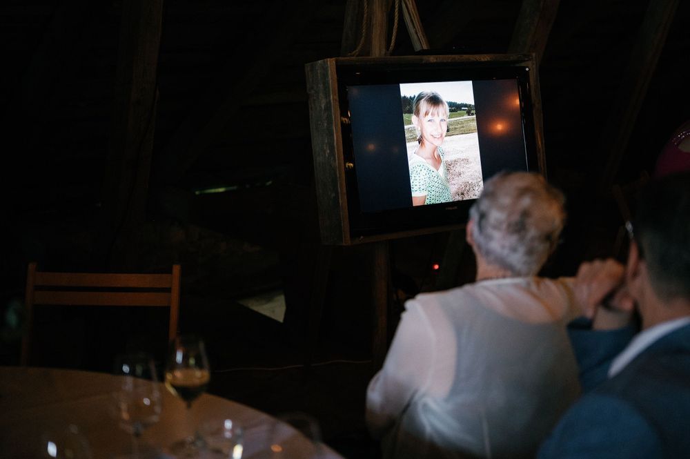 Wedding reception guests watching a presentation on screens in a dimly lit venue.