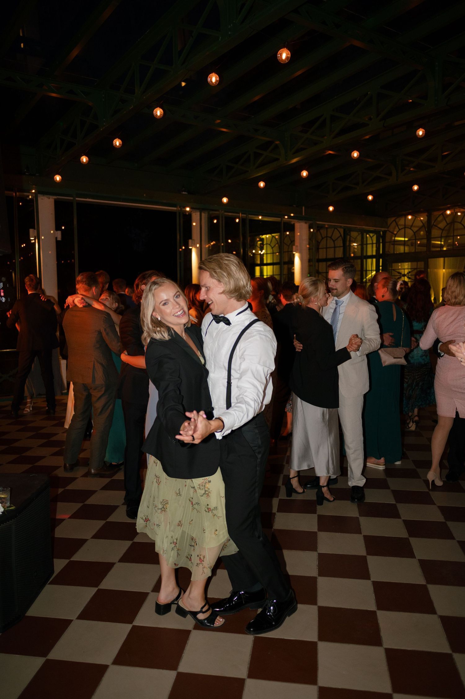 Couples dancing on a black and white checkered floor under ambient lighting at wedding reception.