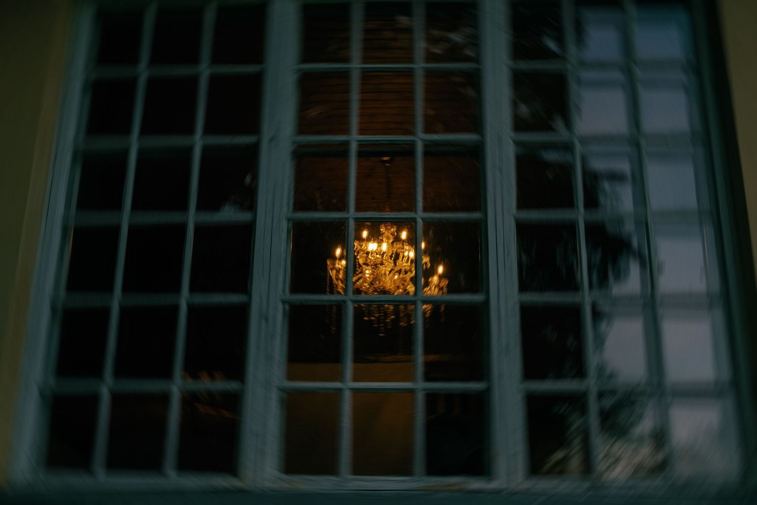 Glowing chandelier seen through a window at night creating a romantic ambiance.