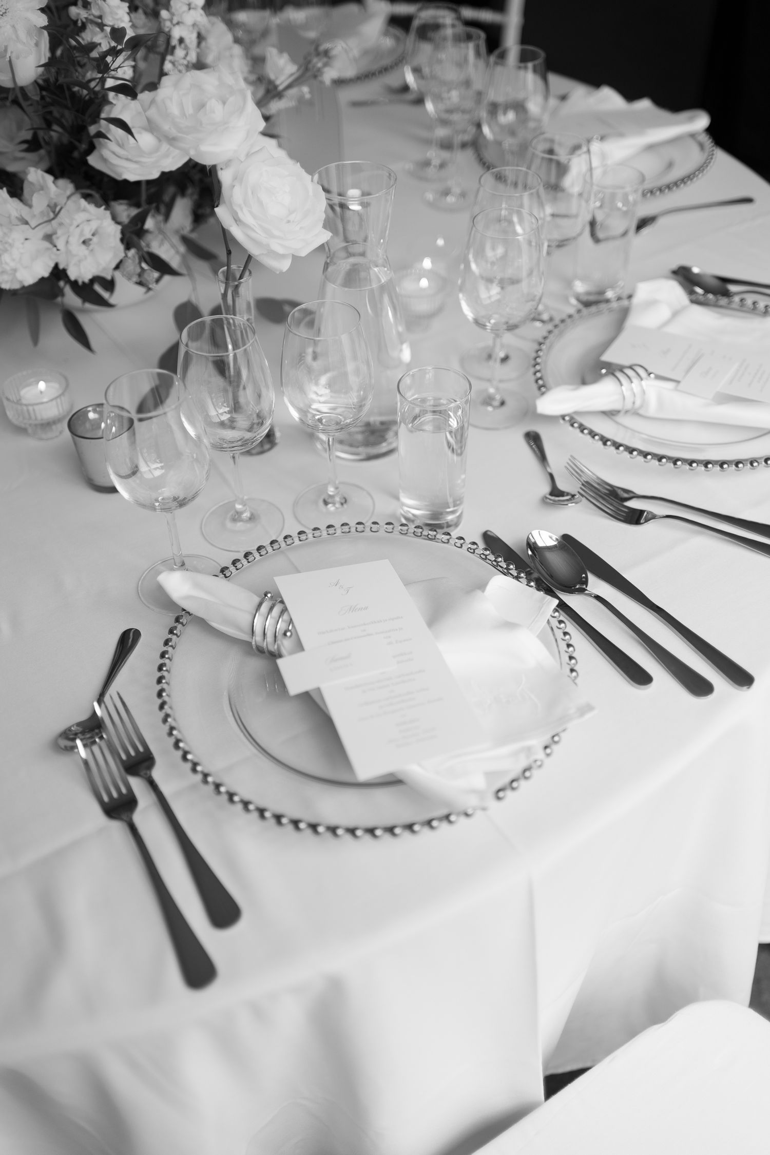 Elegant black and white wedding table setting with beaded charger plates, crystal glassware, silverware, and white floral centerpiece.