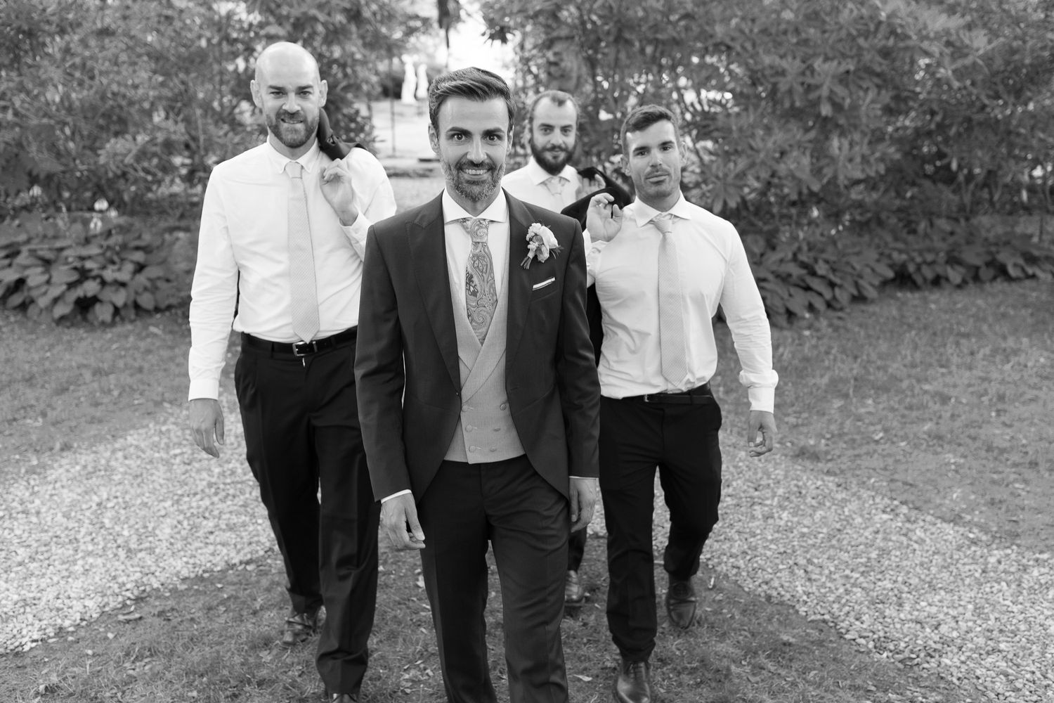 Black and white photo of a groom and three groomsmen walking confidently outdoors at a wedding.