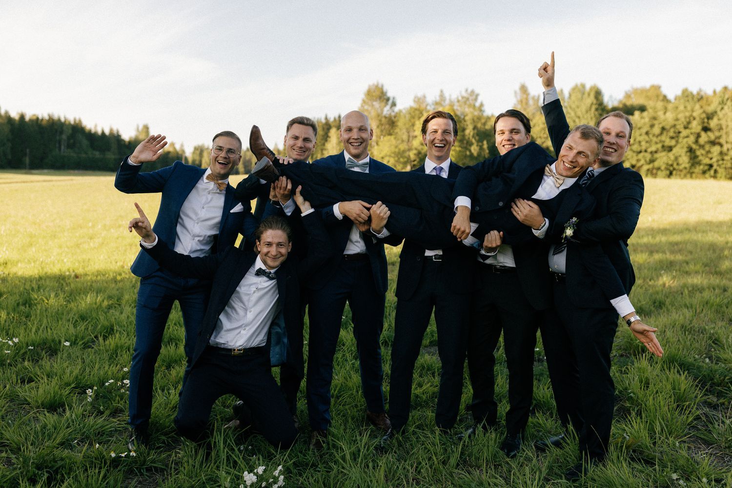 Wedding party jumps joyfully for group photo in outdoor setting.