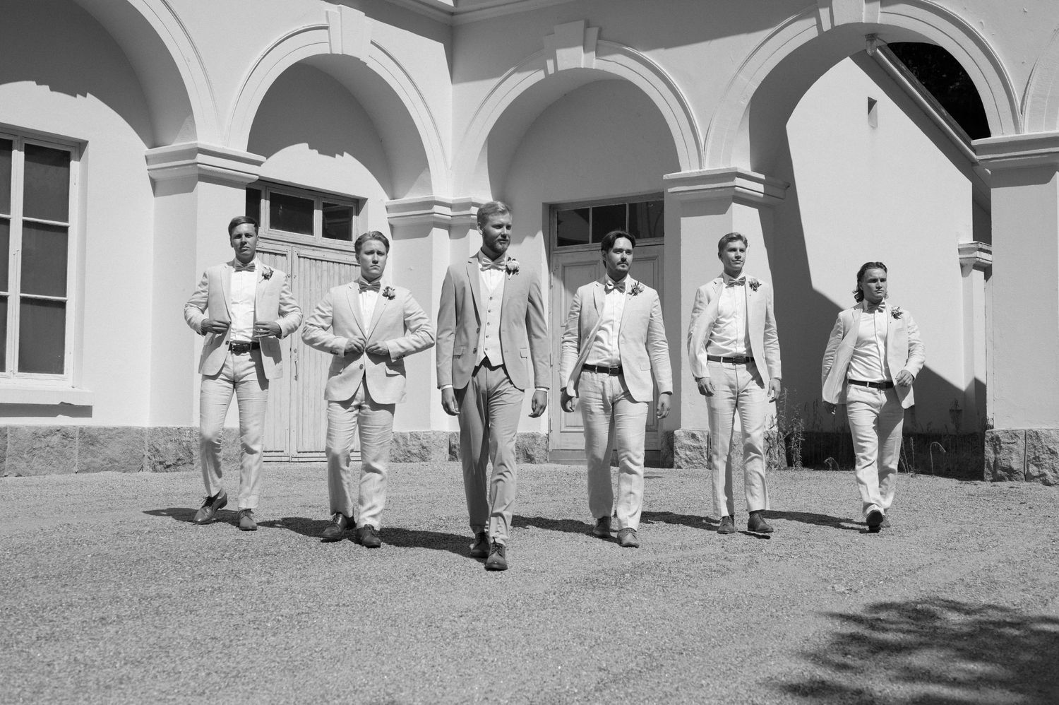 Wedding party in white and pink attire poses on grand columned steps of historic building.