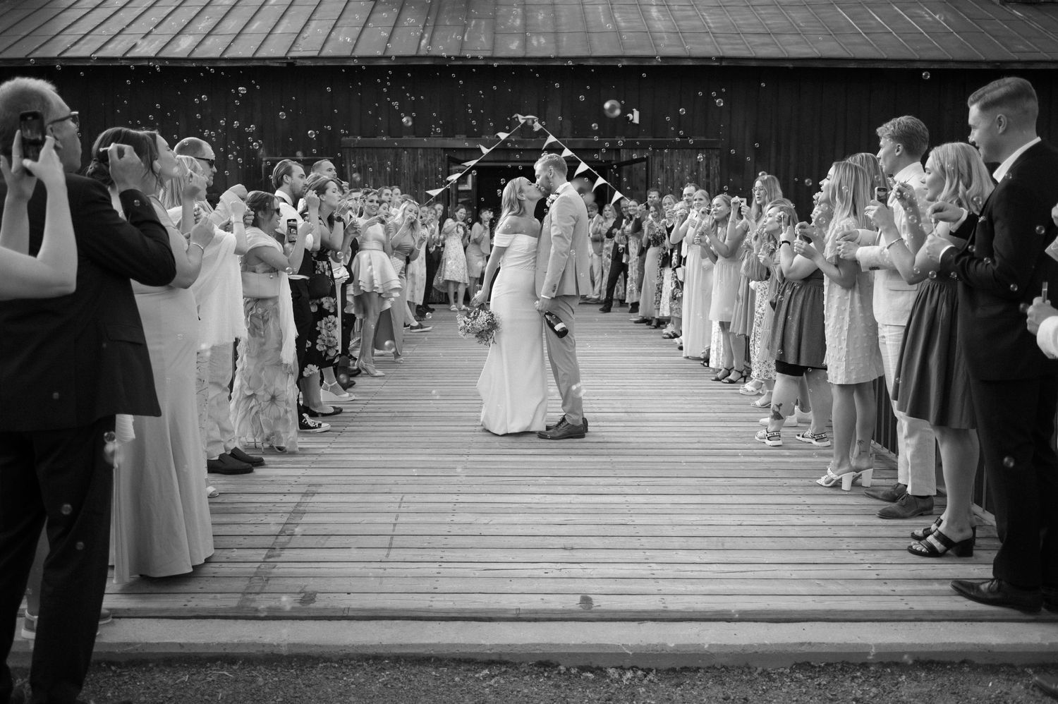 Black and white photo of wedding guests lining a wooden walkway during the celebration.