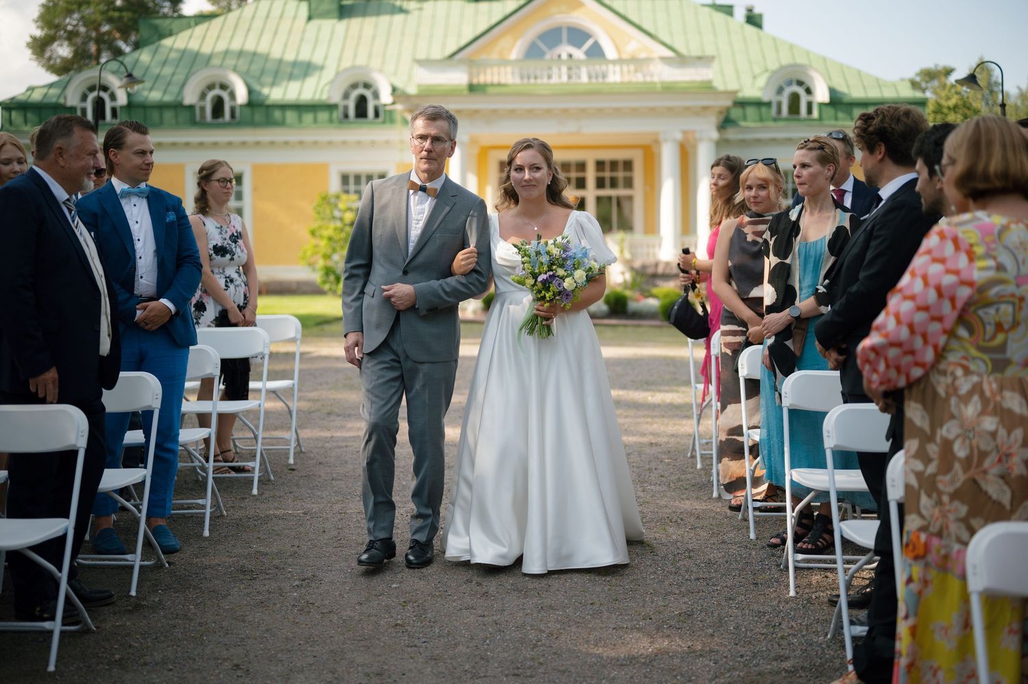 Outdoor wedding ceremony setup with white chairs and yellow mansion in background.