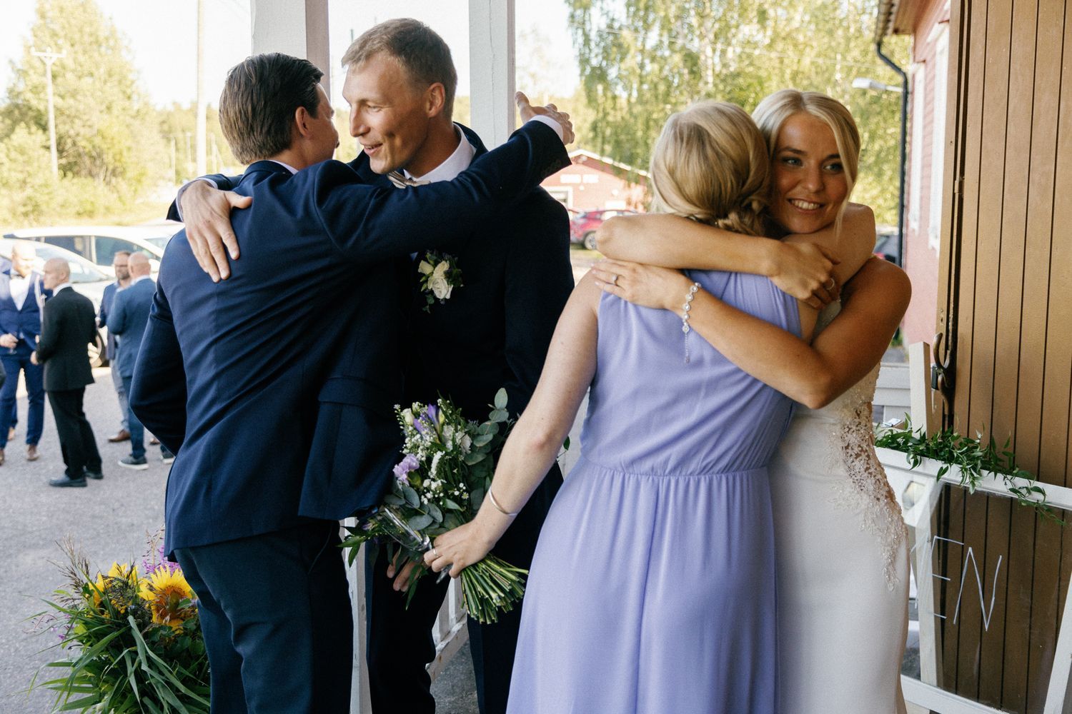 Wedding party members sharing emotional embraces outdoors.