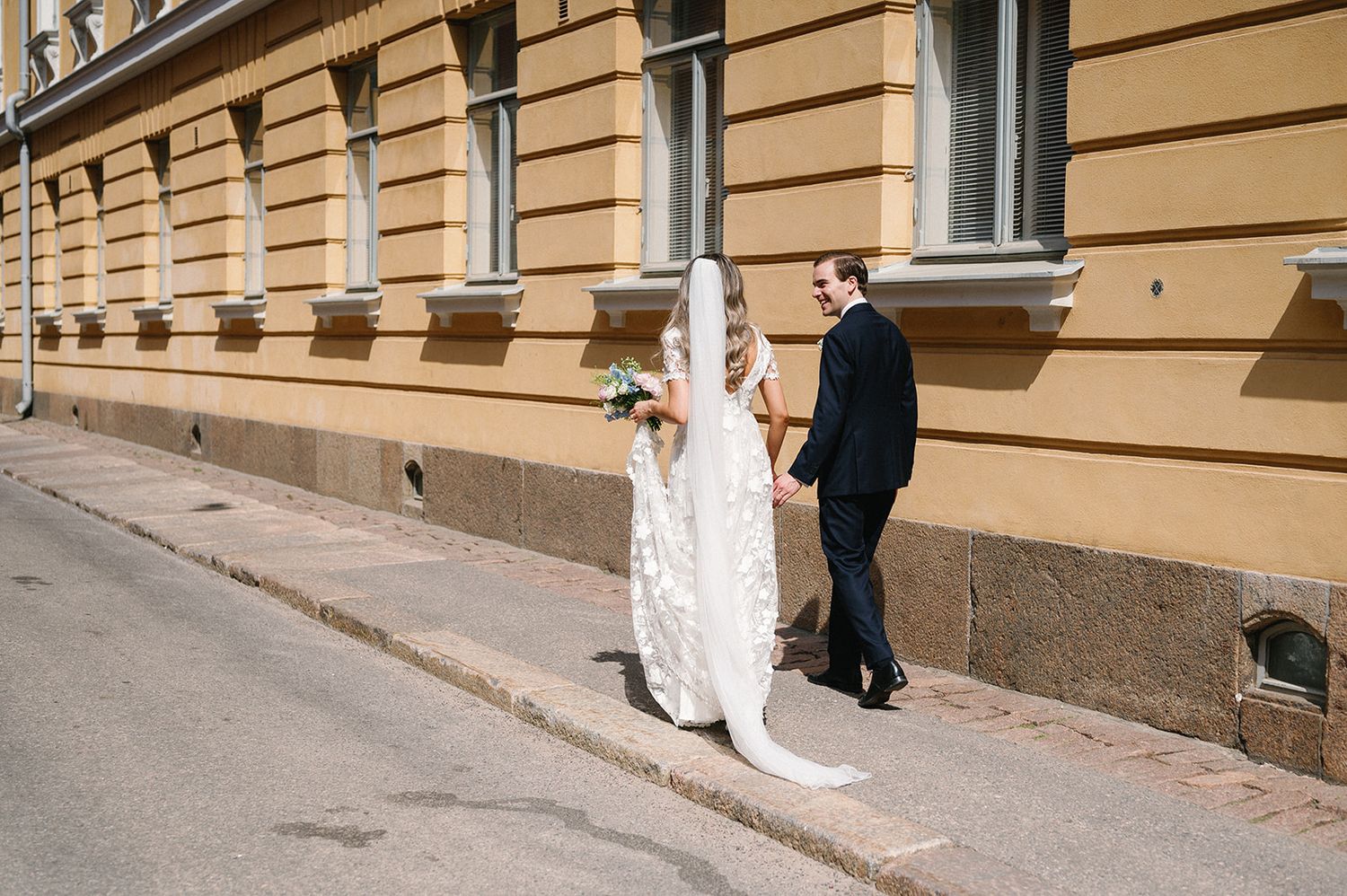 Newlyweds strolling along a yellow-walled historic street.