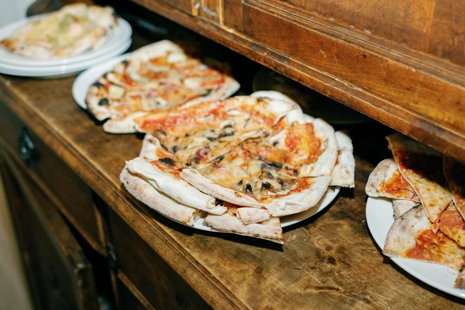 Appetizer platters of flatbread pizza arranged on a rustic wooden buffet table.