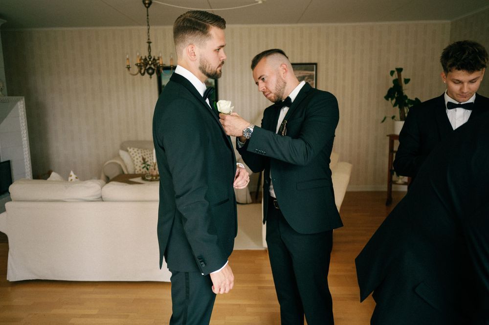 Groomsmen in black suits preparing for wedding ceremony indoors.