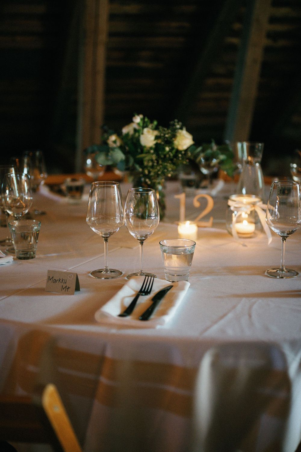 Elegant wedding reception table setting with white linens, wine glasses, and candlelight.