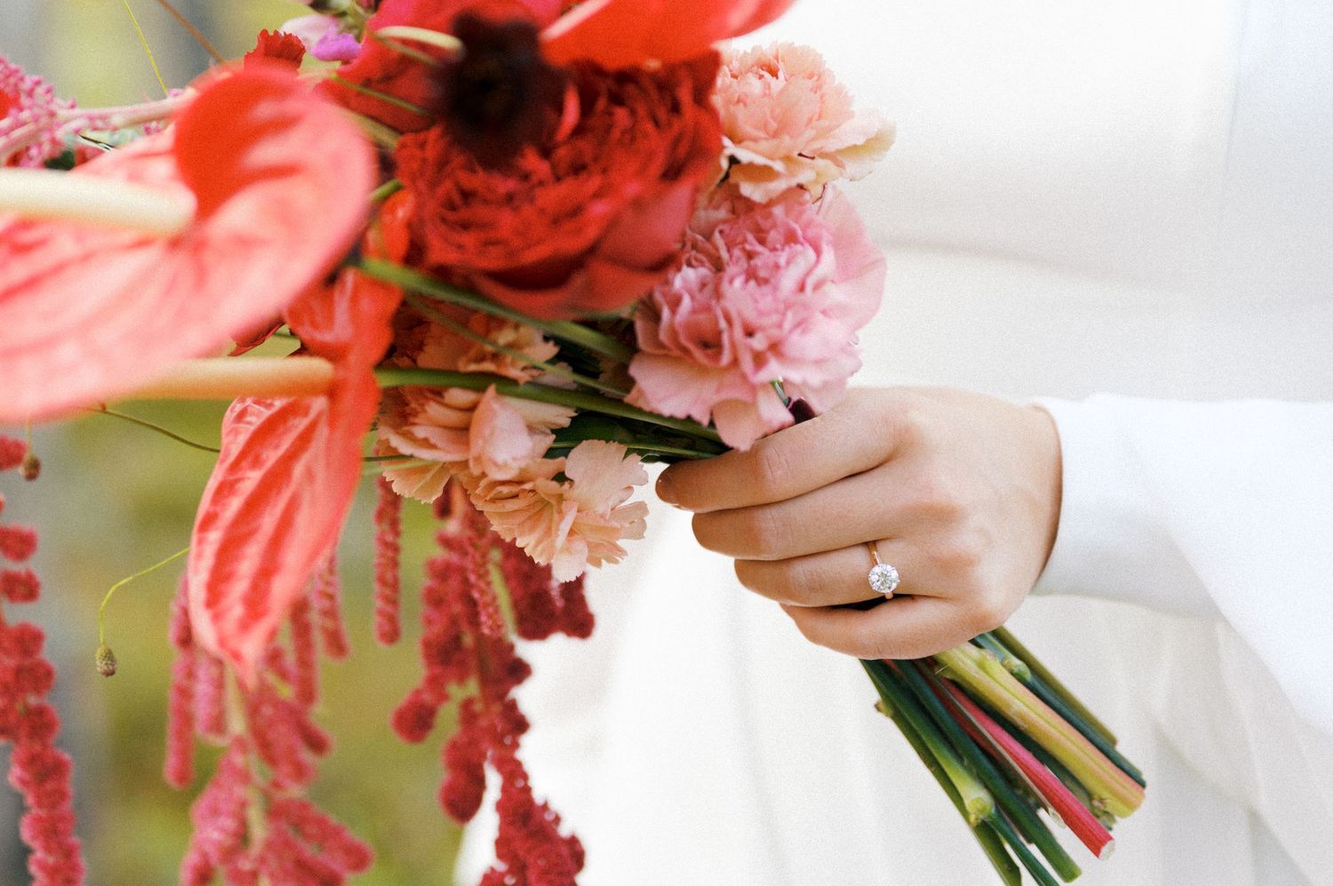Hands holding a vibrant coral and pink wedding bouquet with cascading amaranthus and roses.