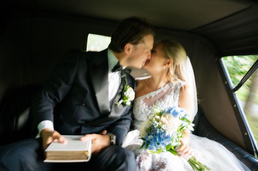 A couple shares an intimate moment in a car on their wedding day.