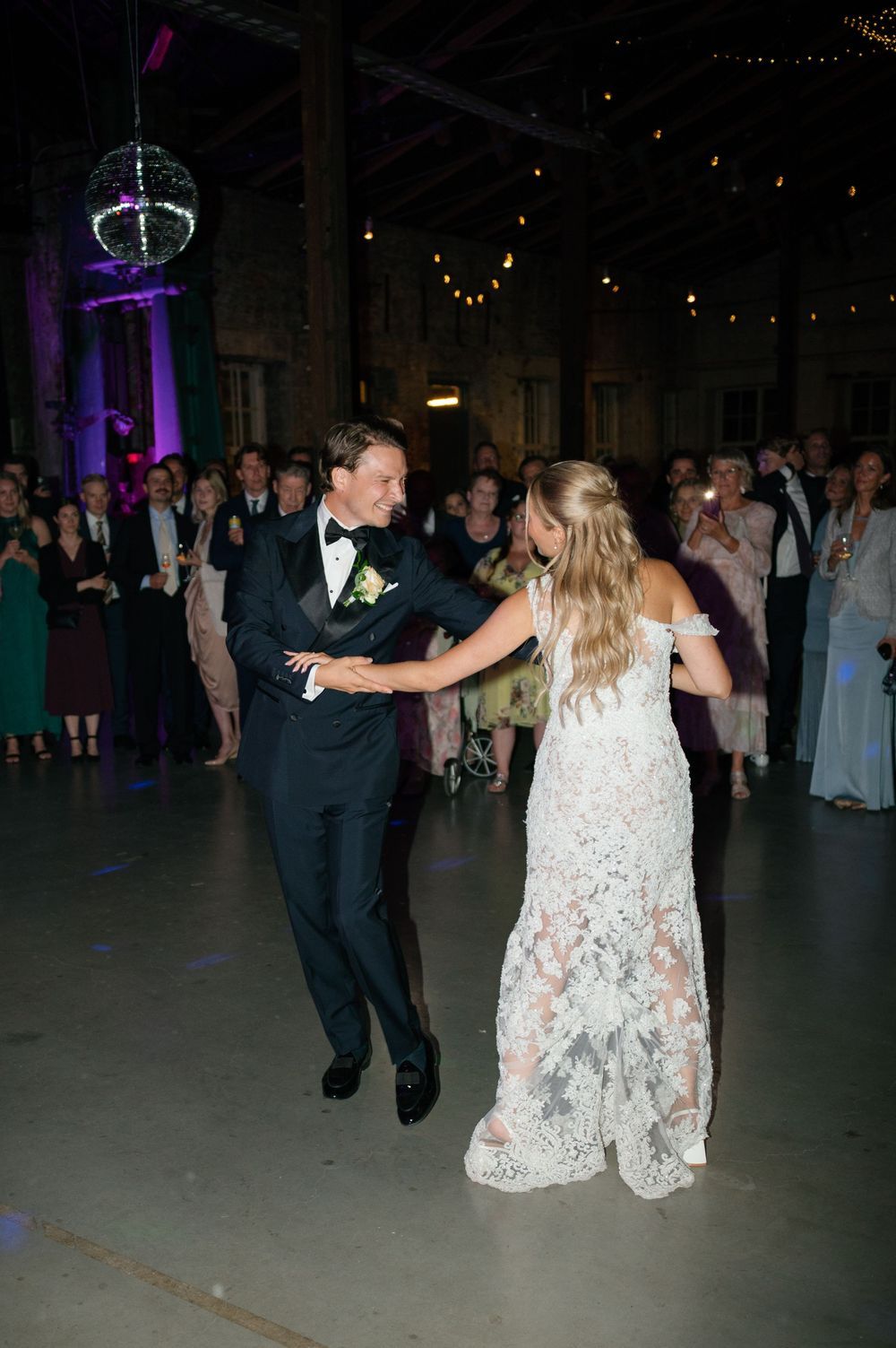 Wedding guests dancing on a dark dance floor under decorative string lights.