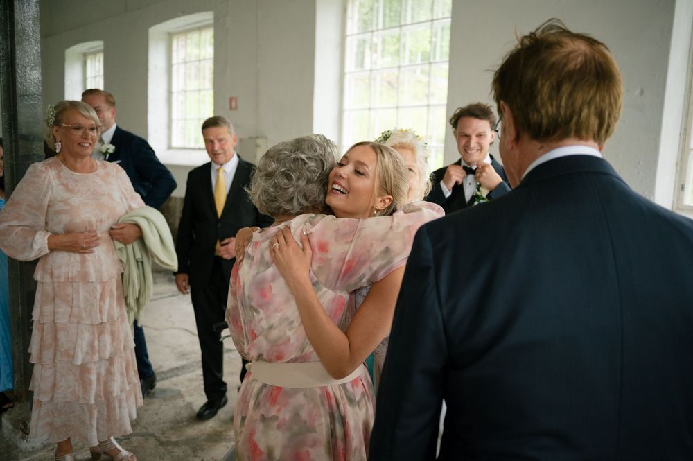 Wedding guests in formal attire dancing and celebrating in an industrial-style venue with large windows.