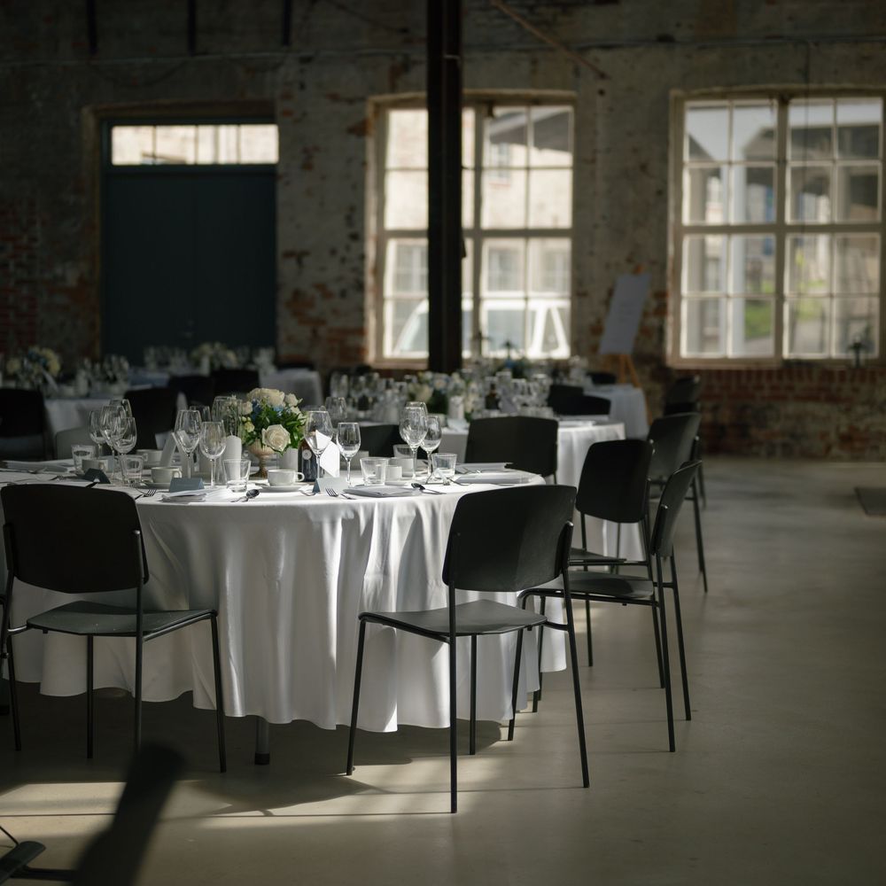 Industrial event space with round tables and modern black chairs set for a formal occasion.