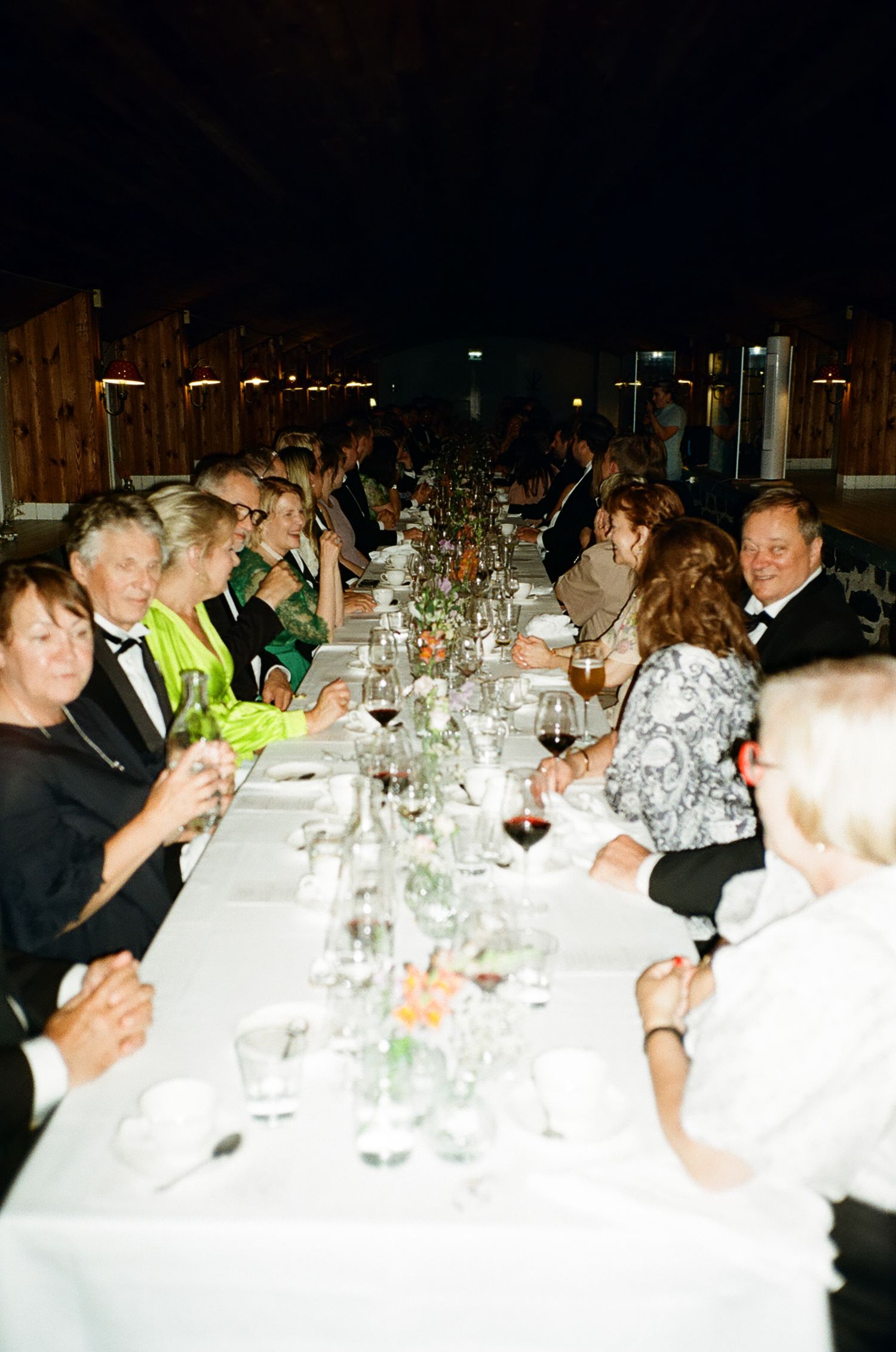 Elegant formal dinner party with guests in black tie attire seated at a long banquet table with white linens.