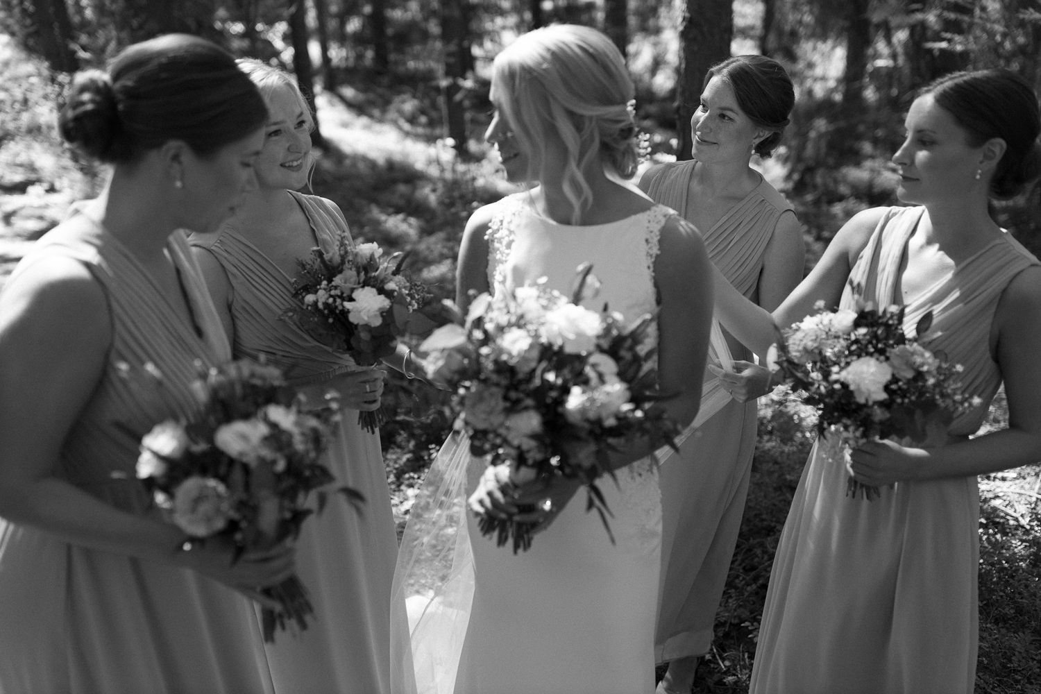 Wedding party members gather closely together holding floral bouquets.