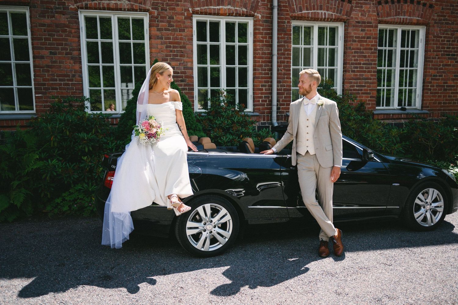 Wedding couple walking near parked car outside brick building venue.