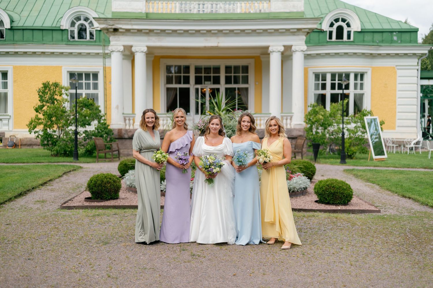 Wedding party poses in front of a yellow and green historic mansion with columned entrance.