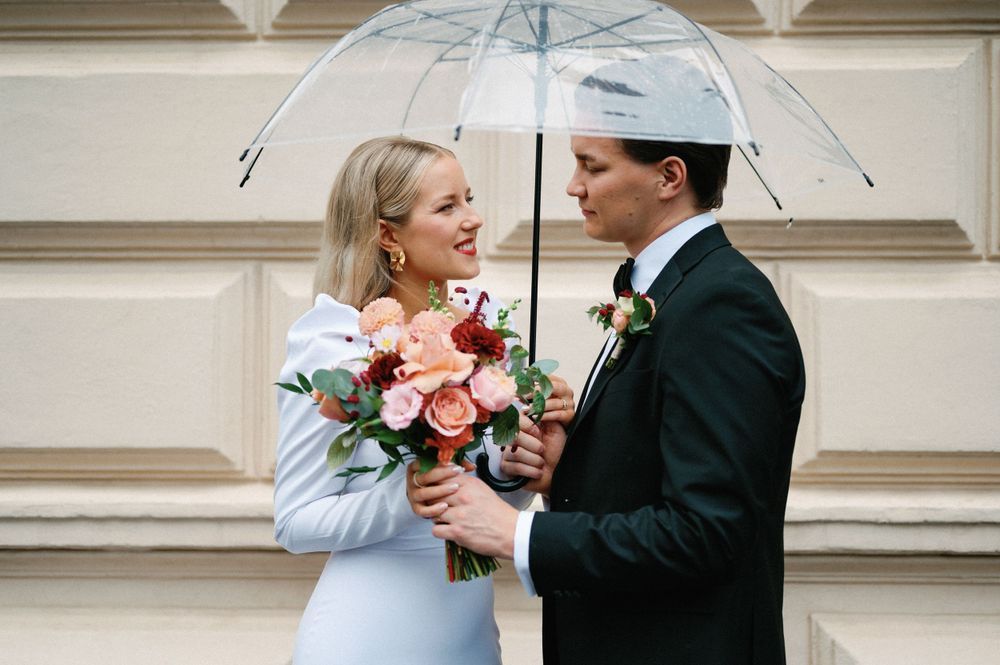 Wedding couple sharing romantic moment under clear umbrella against classic building facade.