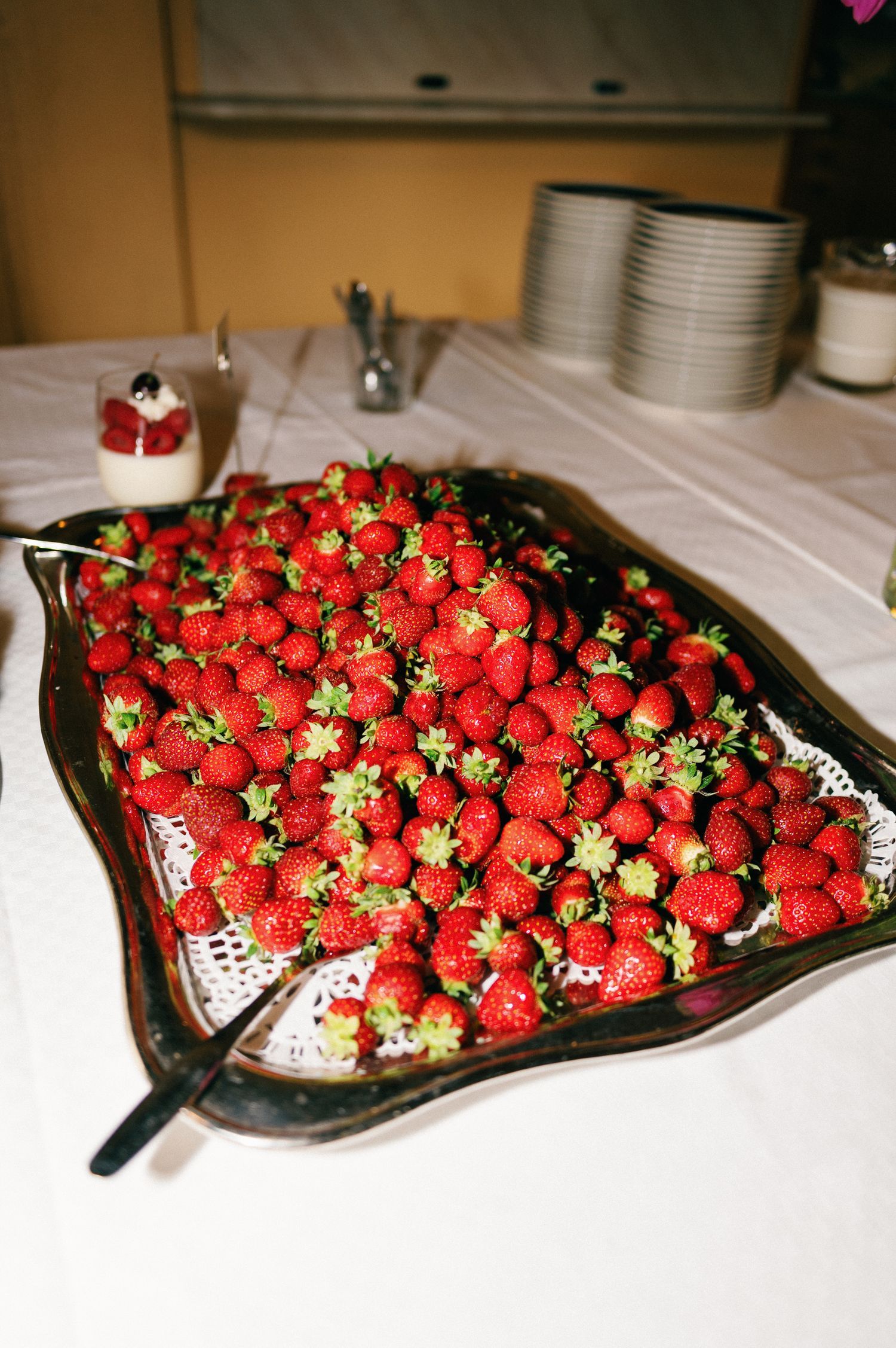 Large platter of fresh red strawberries displayed on white tablecloth at an event.