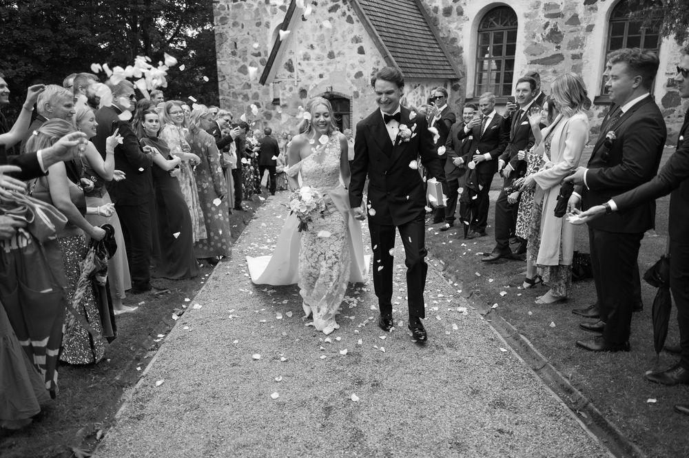 Black and white photo of wedding guests throwing confetti along church pathway.