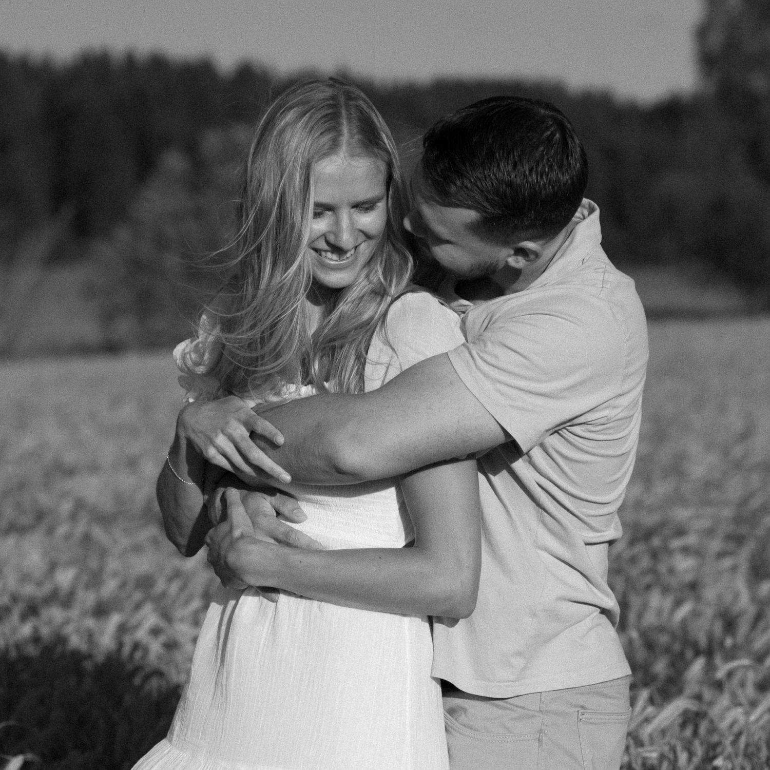 A romantic black and white portrait of a couple embracing in a sunny field.