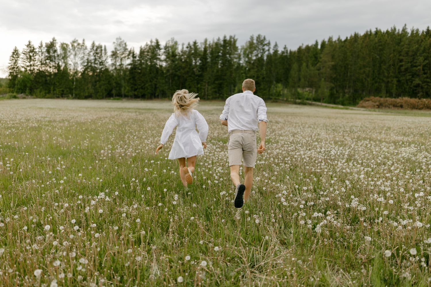 A couple runs through a field of white wildflowers on a cloudy summer day.