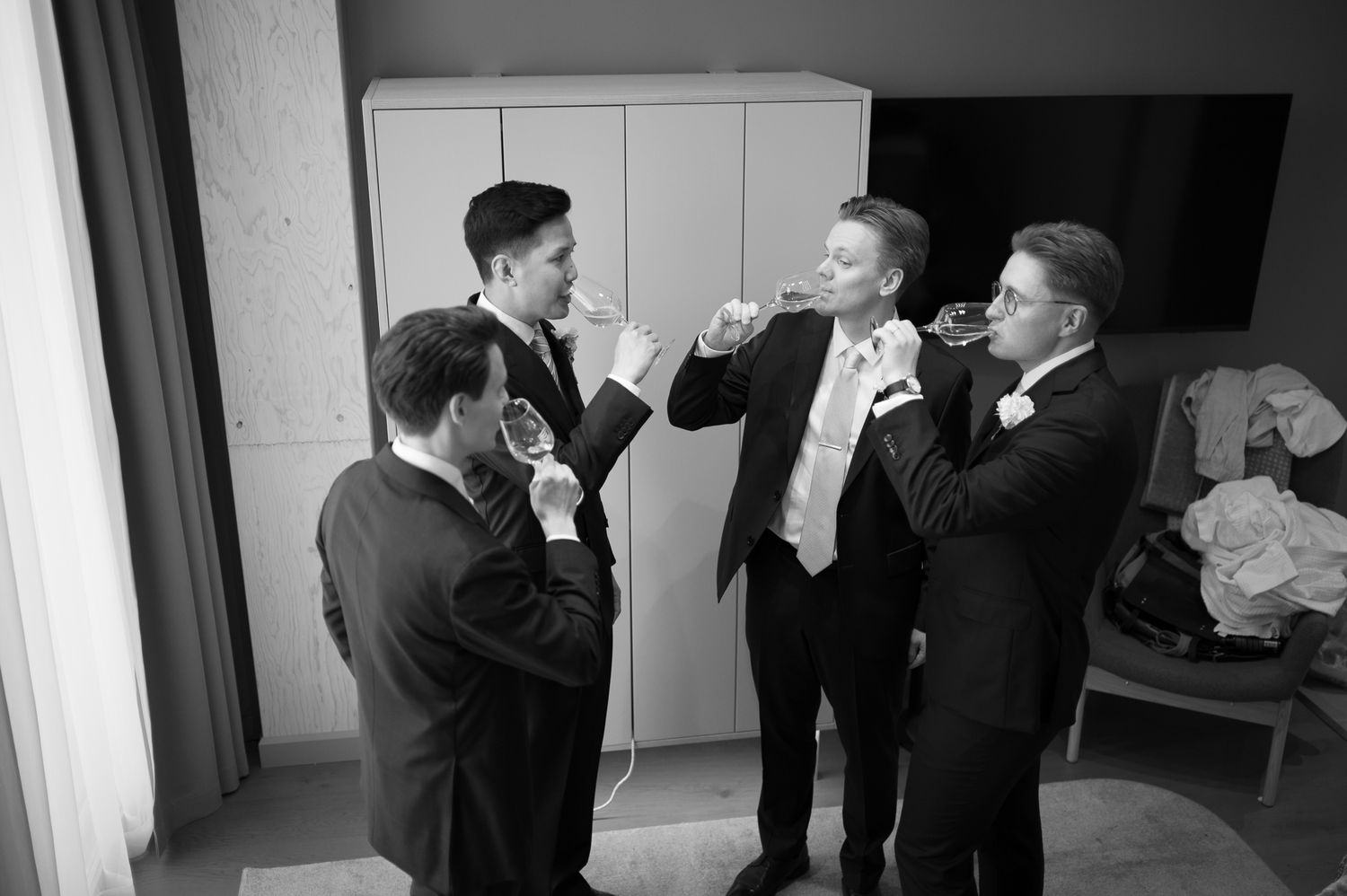 Four men in suits toasting with drinks at a wedding celebration in a modern room.