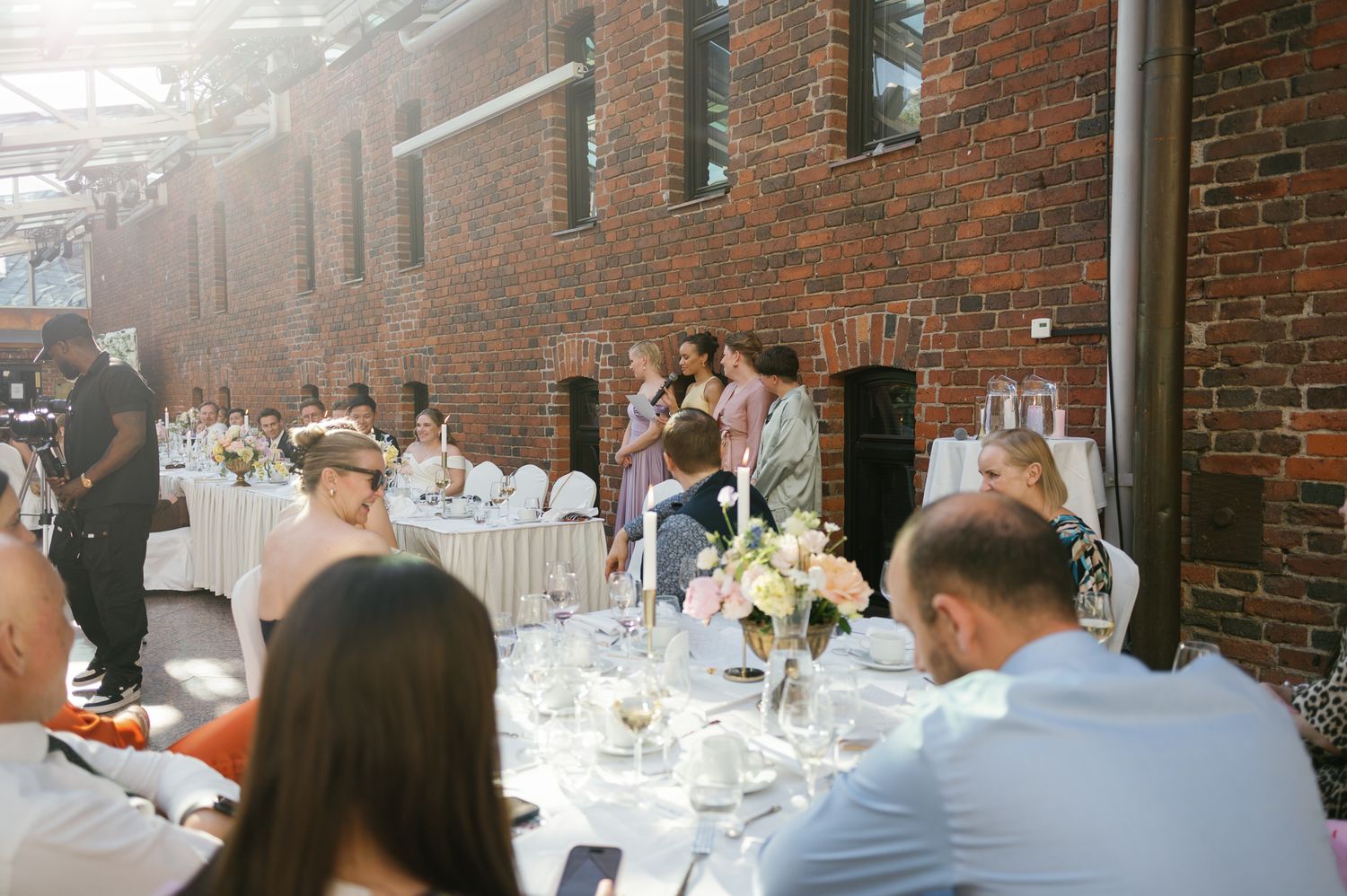 Elegant wedding reception in a brick venue with guests seated at decorated tables with floral centerpieces.
