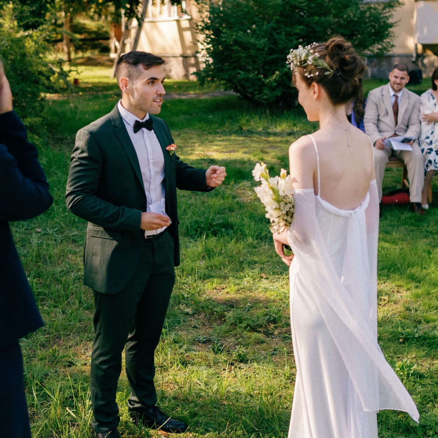 An elegant outdoor wedding ceremony unfolds on a grassy lawn with a historic yellow building backdrop.