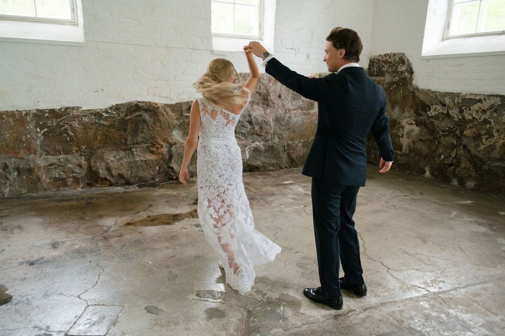 Dancing couple twirl gracefully in a rustic room with windows and exposed stone walls.