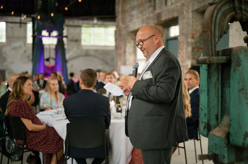 Reception guests mingling in historic venue with exposed brick walls and large windows.