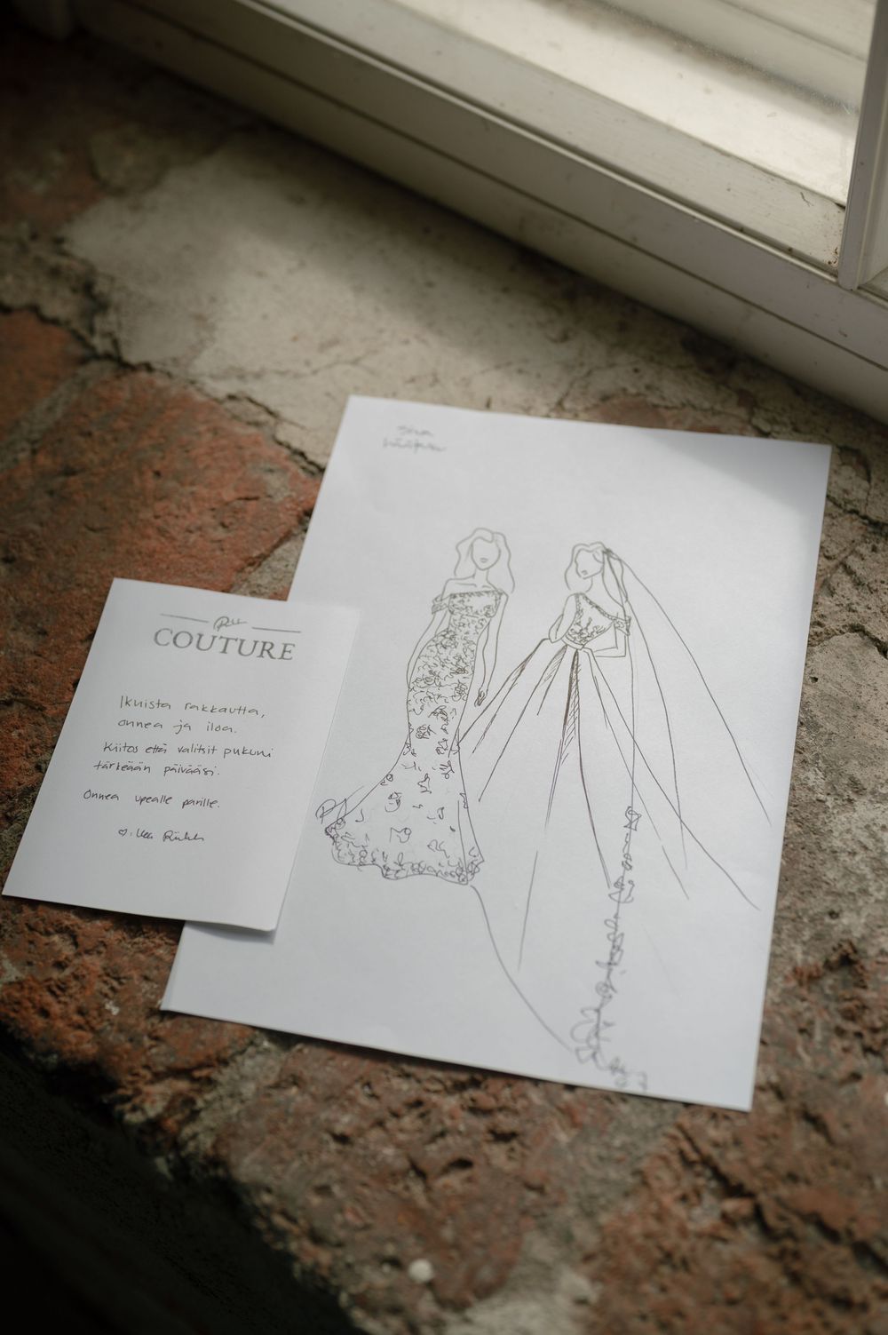 Wedding dress design sketches laid out on a rustic brick surface.