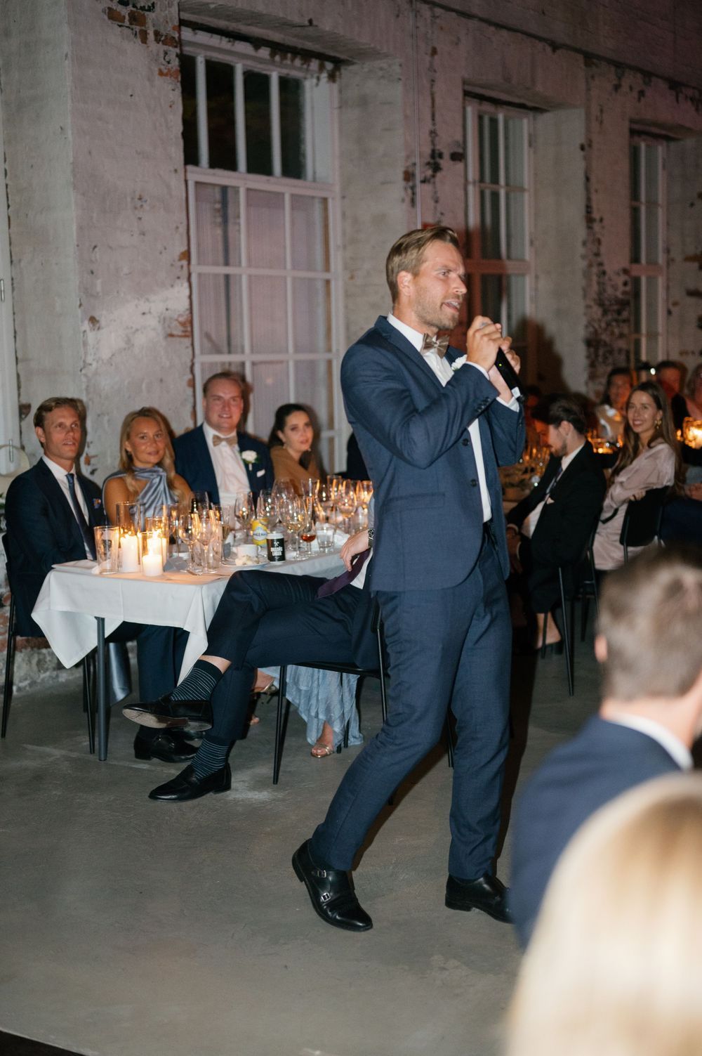 Wedding guests dancing energetically in formal attire at an elegant indoor reception with candlelit tables.