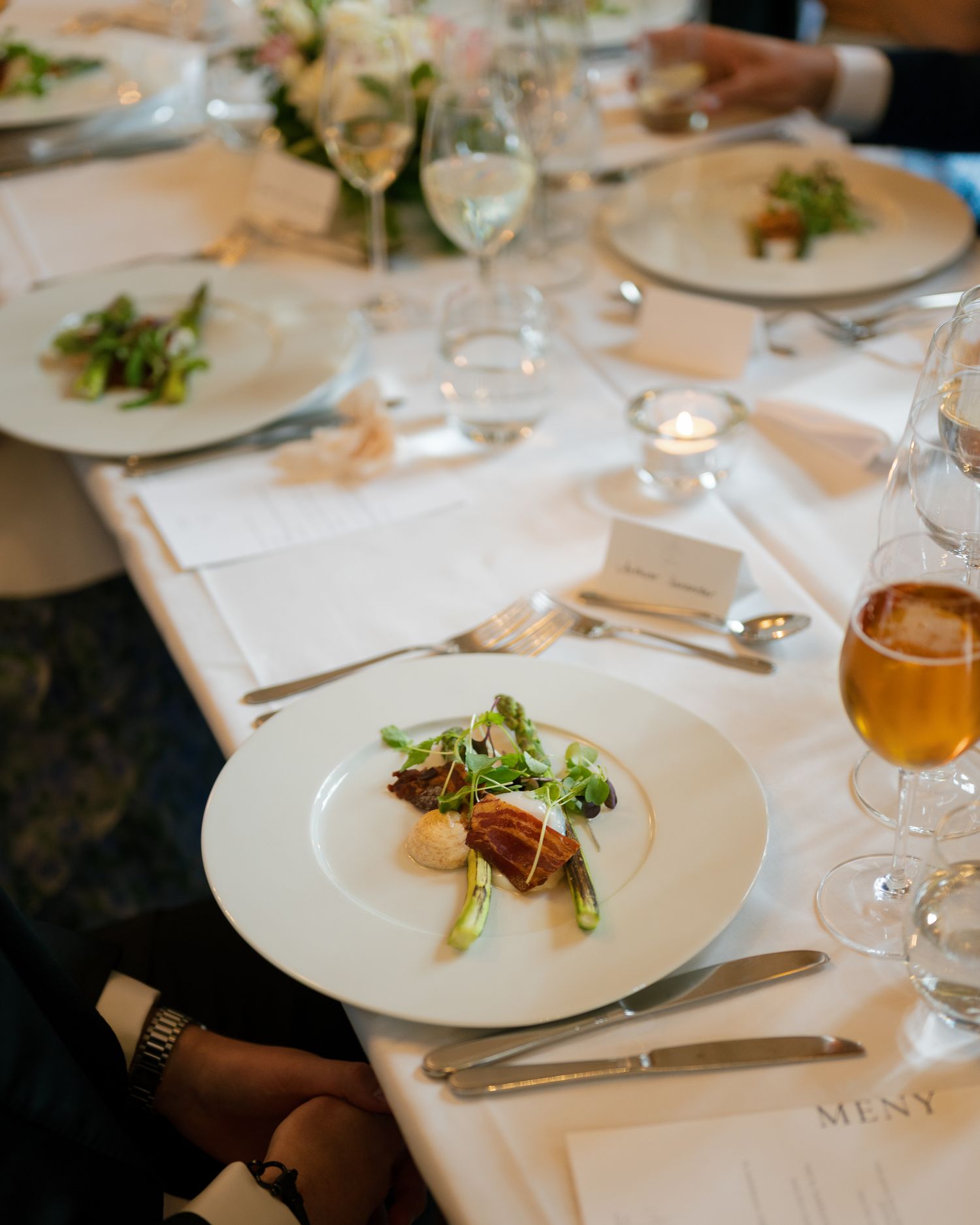 A fine dining table setting with multiple white plates, wine glasses, and delicate plating of gourmet dishes.