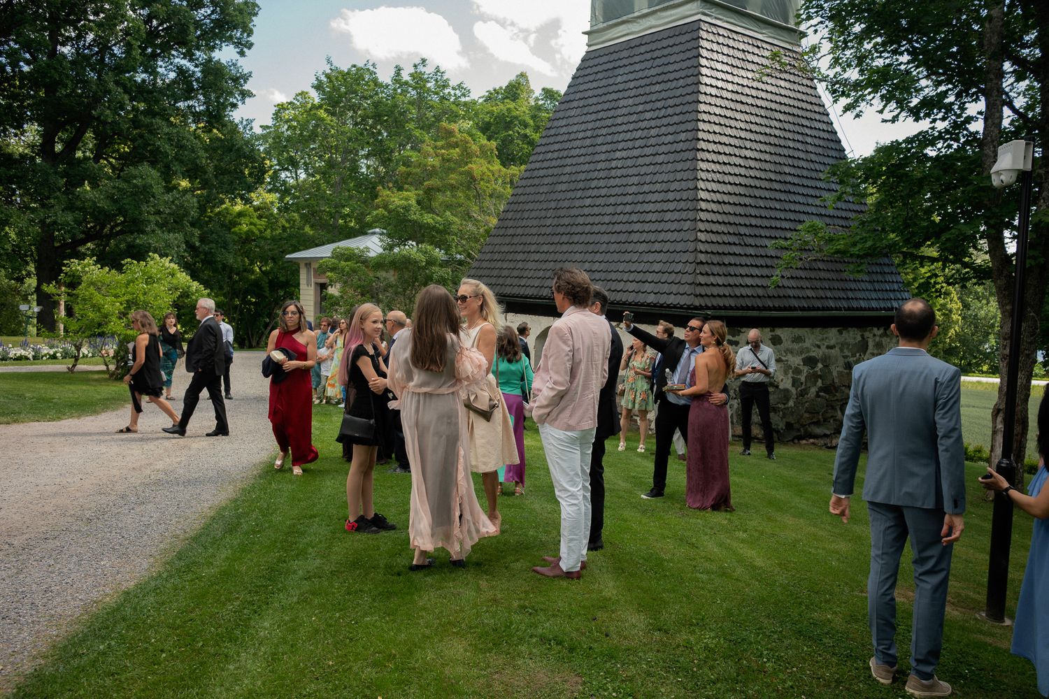 Guests mingling outdoors on green lawn near historic chapel during elegant wedding cocktail hour.