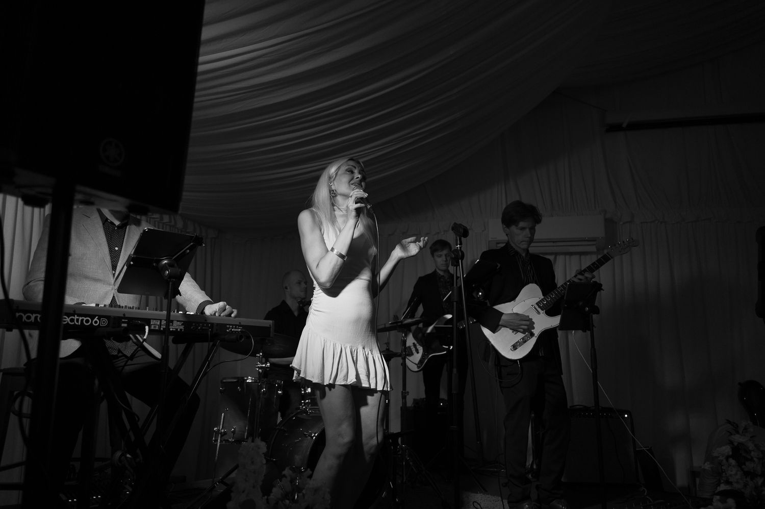 Black and white photo of a female singer performing on stage with guitarist and keyboardist at a live music event.