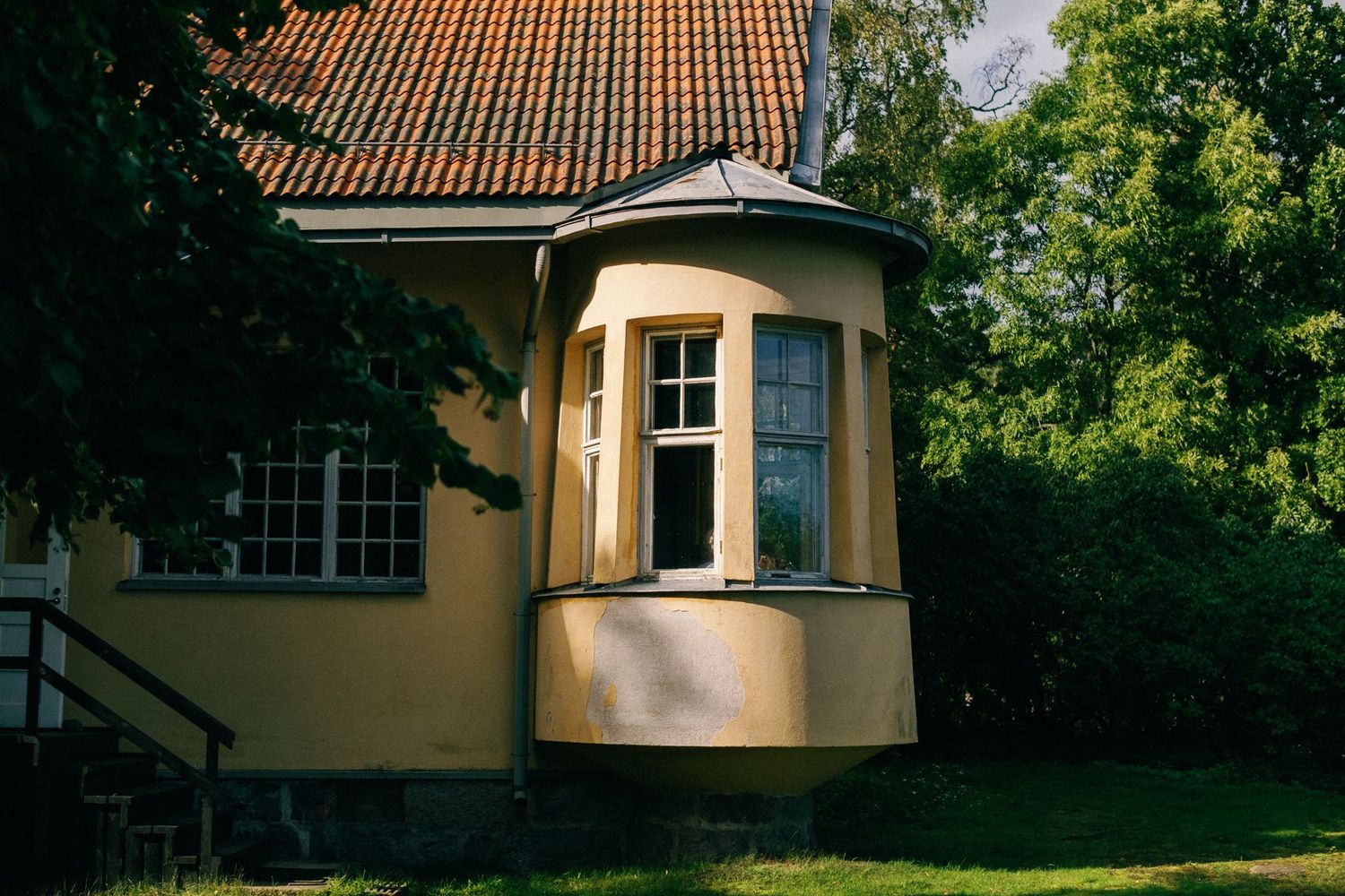 Yellow stucco building with terracotta roof tiles and bay windows in a garden setting.