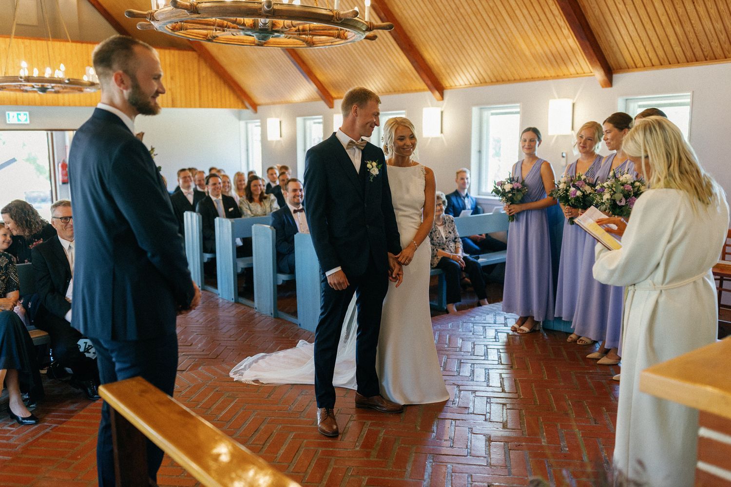 A wedding ceremony takes place inside a rustic chapel with wooden beams and natural lighting.