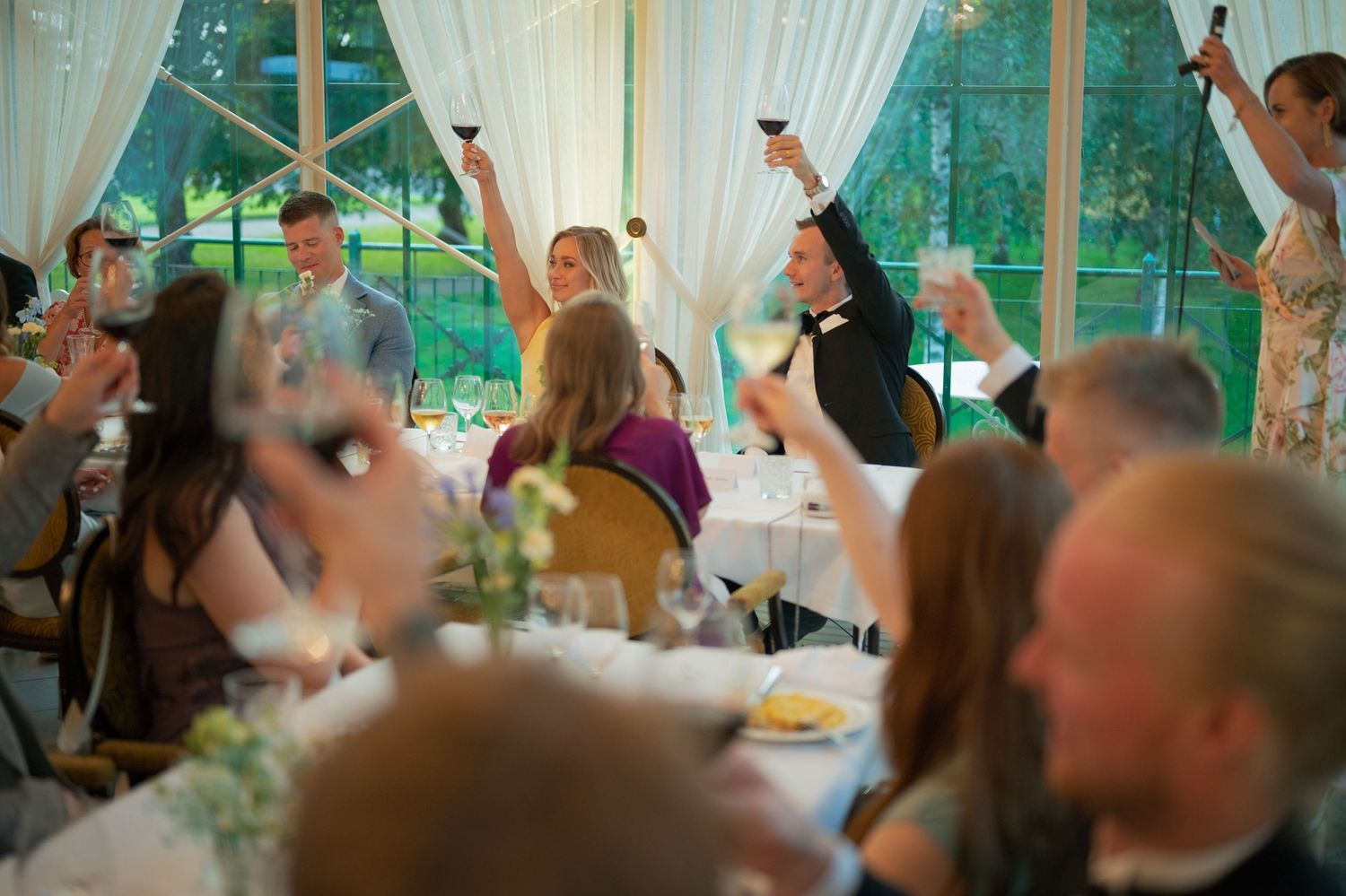 Wedding celebration in a glass-walled venue with white draping and natural light.