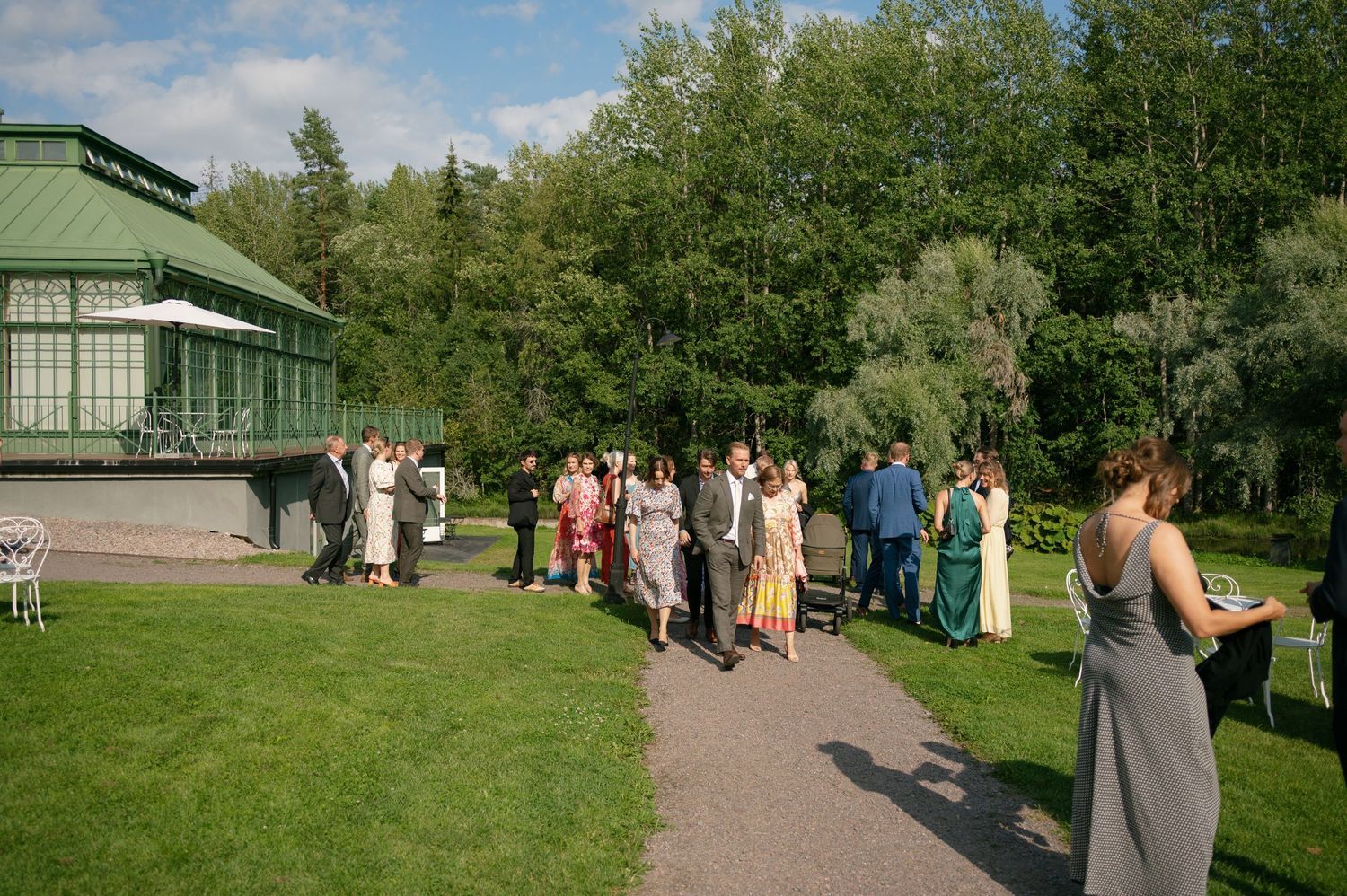 Outdoor gathering on a path near a white building surrounded by lush greenery.