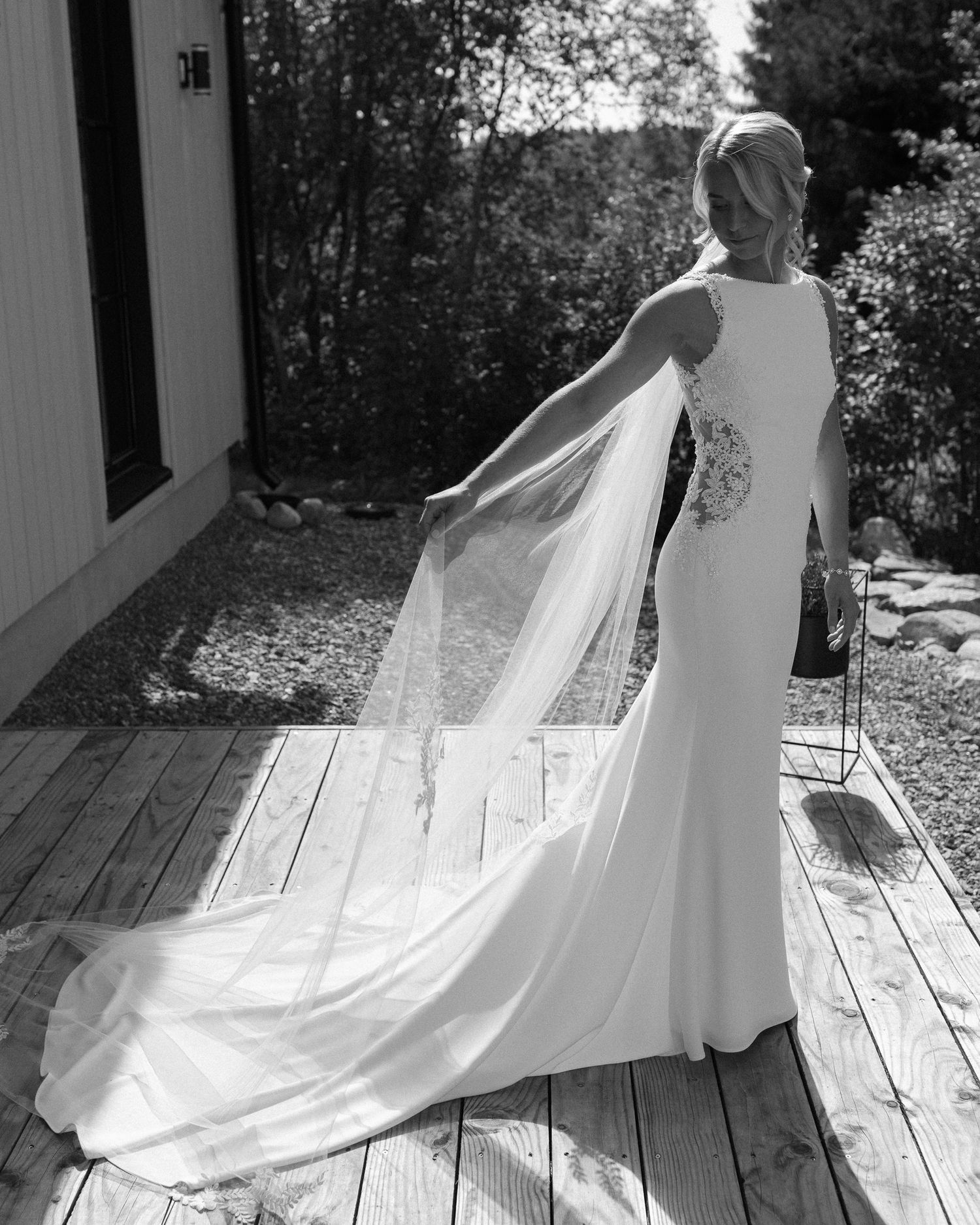 Wedding dress with flowing train captured in black and white on wooden deck.