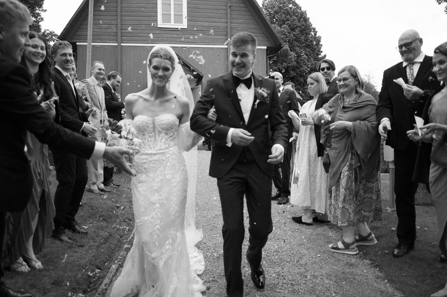 Guests line up along a path near a rustic barn for a wedding celebration.